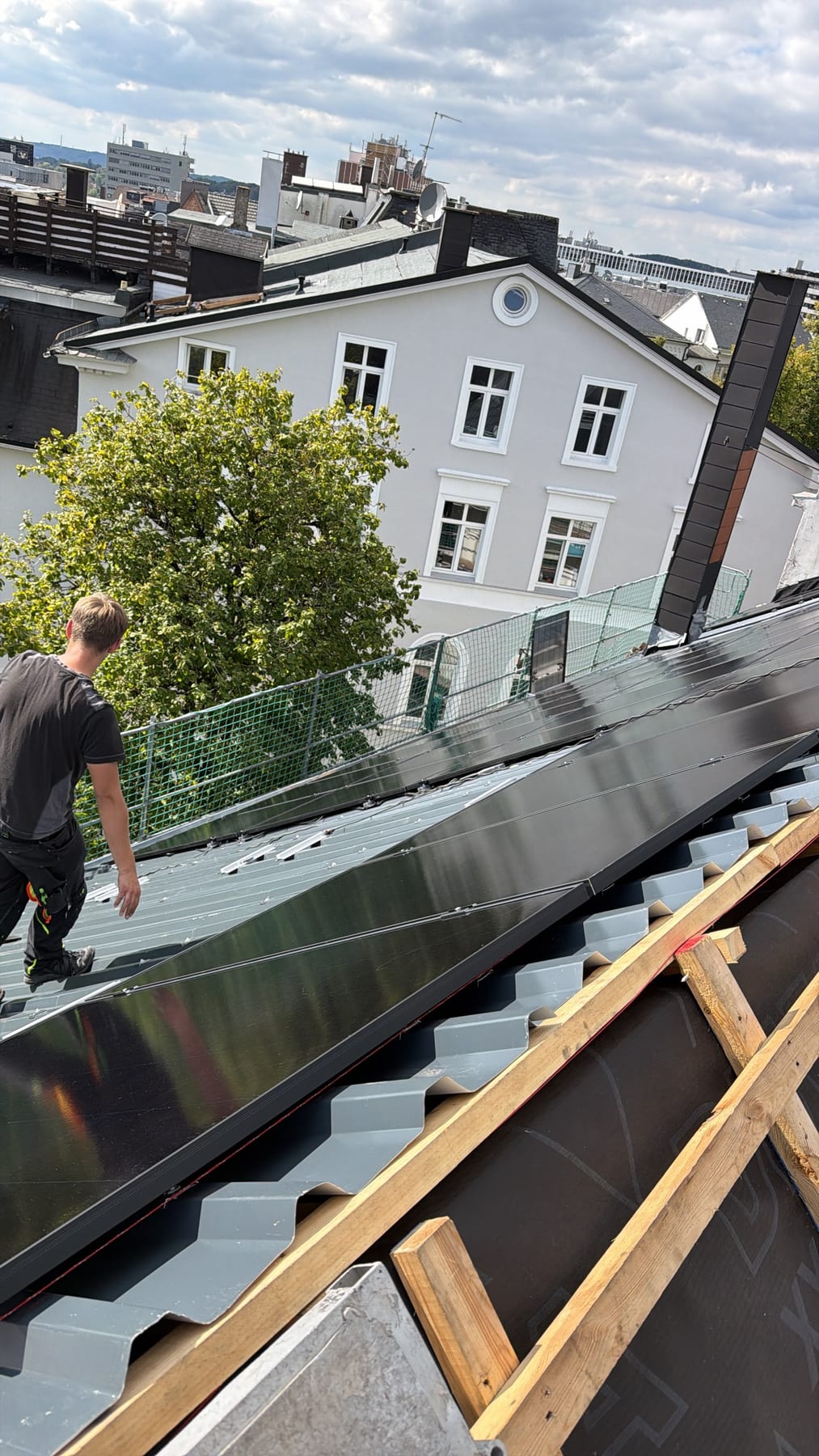 Eine fertige Modulreihe auf dem neuen Metalldach, ein Monteur geht daneben entlang