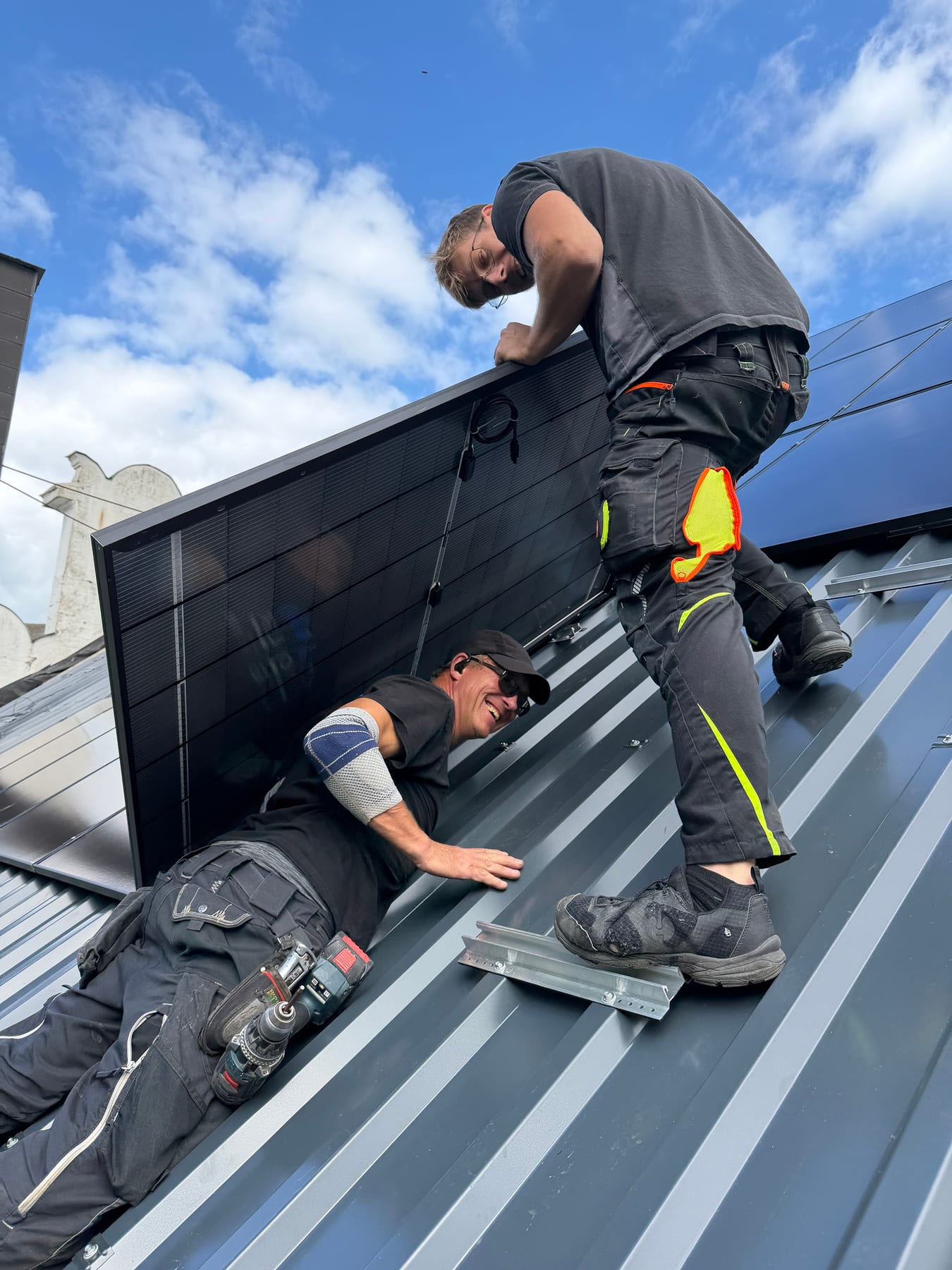 Zwei Handwerker setzen zu zweit ein Photovoltaikmodul auf die montierten Schienen des neuen Metalldachs
